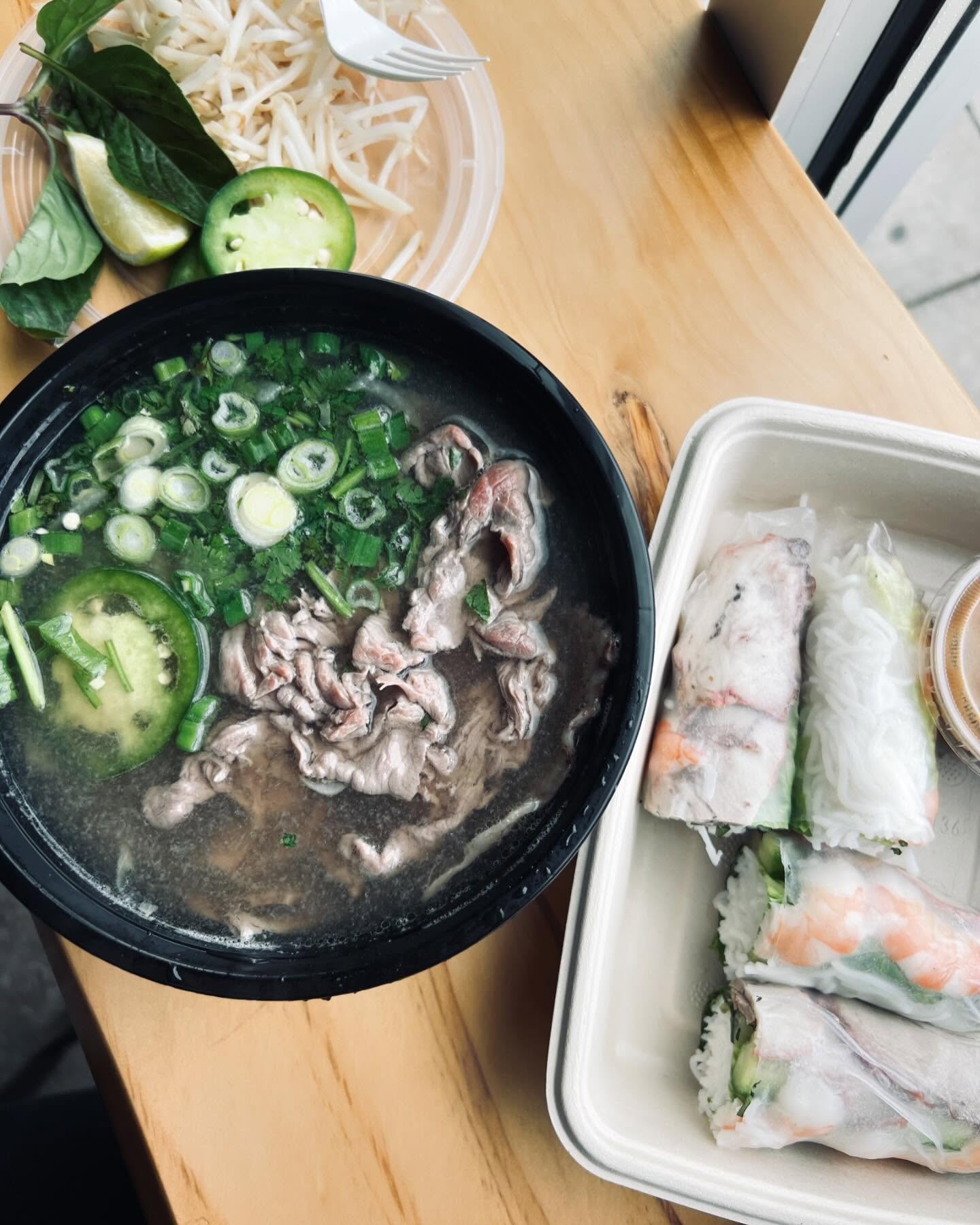 Steaming phở bowl with fresh herbs and spring rolls at La Cà Café